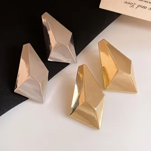 Macro view of gold and silver minimalist geometric faceted metal stud earrings on a dual background