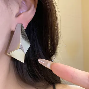 Close-up detail of a large silver geometric faceted stud earring worn on a model's ear