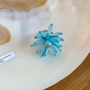 Nahaufnahme eines blauen Acryl-Blumenrings mit aufwendigen Perlendetails auf einer Muschel