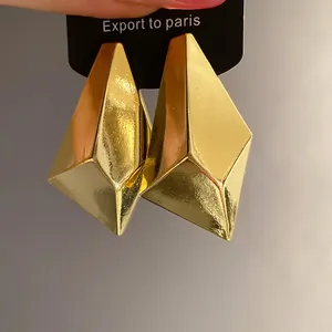 Close-up of golden geometric-cut stud earrings with a glossy vintage finish.