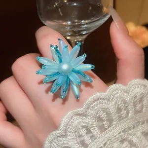 Nahaufnahme eines blauen Acryl-Blumenrings mit einer zentralen Perle an einer Hand.