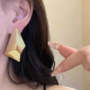 Close-up of a fashion model wearing large geometric gold faceted minimalist stud earrings