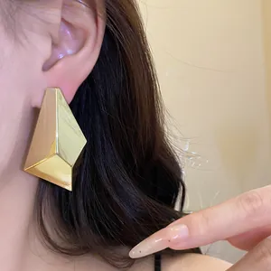 Close-up detail view showing the metallic texture of a geometric faceted gold stud earring