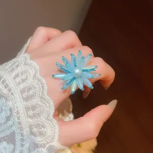 Detaillierte Nahaufnahme eines blauen Blumenrings aus Acryl mit Perle auf der Hand