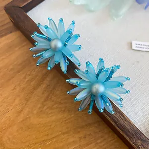 Makroaufnahme von blauen Acrylblumen-Ohrringen mit Perlenzentrum und Glasperlen