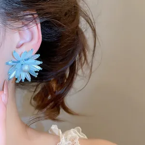 Detailansicht eleganter blauer Acryl-Blumenohrringe mit Perle am Ohr getragen