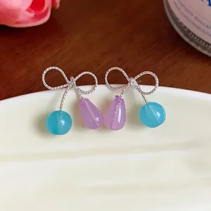 Primo piano di dolci orecchini a fiocco in argento con perle di resina blu e lilla.