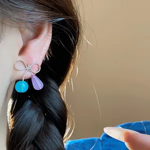 Primo piano di orecchini a fiocco con gocce in resina blu e viola indossati su modella