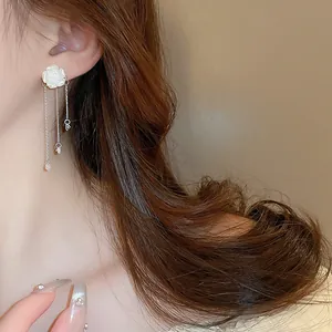 Close-up detail view of elegant white acrylic flower earring with delicate metal tassels on ear