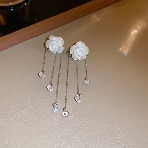 Close-up of white acrylic rose earrings with dangling gold-tone tassels and crystals.