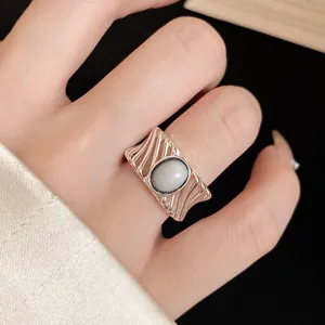 Close-up detail of a retro hollow silver ring with an oval grey stone on a finger.
