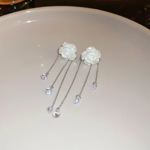 Close-up of elegant white acrylic rose tassel earrings with shimmering crystals.
