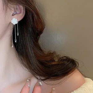 Detail shot of elegant acrylic white flower earrings with dangling silver tassels