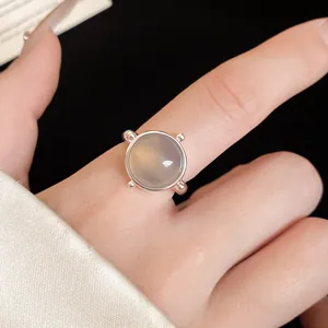 Detailed view of a silver open ring with a round translucent grey stone on a finger.