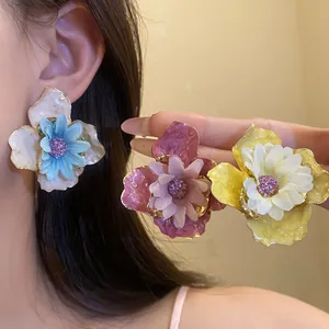 Detalle de cerca de los grandes pendientes de flores 3D de tela y esmalte de verano