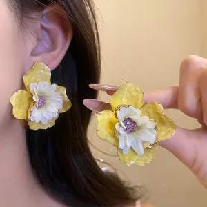 Primer plano de pendientes de flores amarillas con centro de margarita blanca para verano.