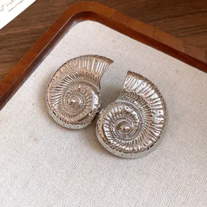 Primer plano de pendientes de caracola plateados vintage con textura en espiral
