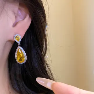 Primo piano dettagliato di orecchini a goccia con zircone giallo e bordi in pavé di cristalli
