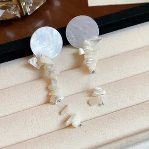 Primer plano de pendientes estilo veraniego con fragmentos de concha en un joyero de tela.