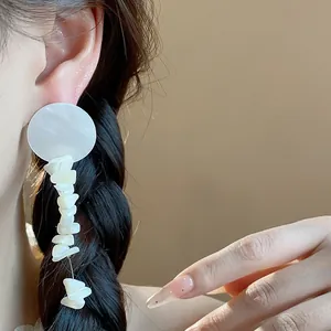 Primer plano de pendientes de concha blanca irregulares llevados por una modelo en verano.