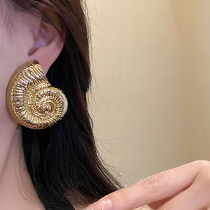 Detalle de un pendiente vintage con forma de caracola dorada llevado por una modelo femenina