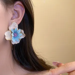 Vista detallada de pendientes florales con flor de seda azul y pétalos de esmalte crema