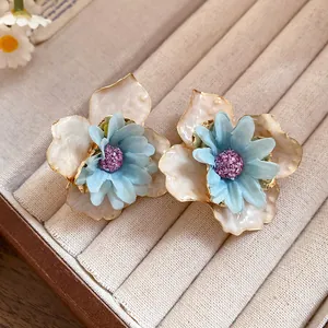 Primer plano detallado de pendientes de flores de tela azul claro y pétalos de esmalte.