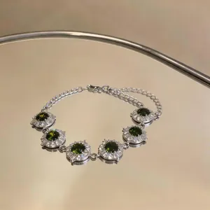 Primo piano di un braccialetto in argento con zirconi rotondi verdi su una superficie a specchio.