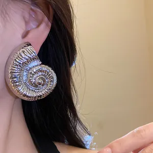 Primer plano de un gran pendiente vintage de concha de nautilus plateada en la oreja.