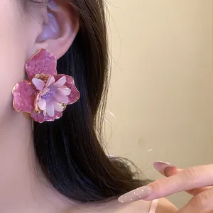 Primer plano de pendientes de flor rosa con pétalos de tela y elegantes bordes dorados.