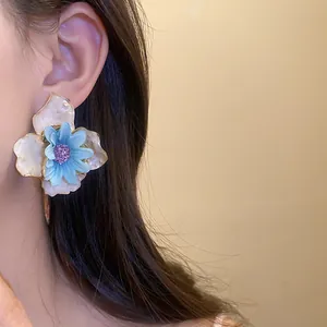 Primer plano de un elegante pendiente floral azul y blanco con centro púrpura en la oreja