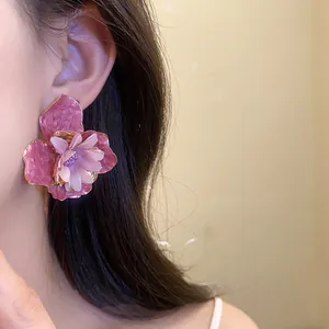 Vista detallada de un elegante pendiente de flor esmaltada rosa en una modelo femenina