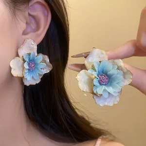 Vista detallada de pendientes de botón con flores de tela azul y crema para vacaciones de verano.