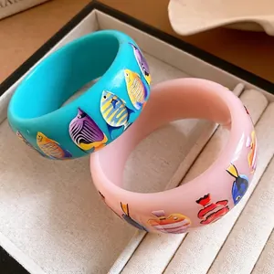 Stylish wide resin bangles with colorful tropical fish prints for vacation outfits.