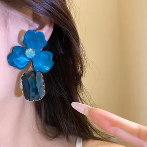 Close-up of blue acrylic flower drop earrings with faceted dark blue gemstone pendant