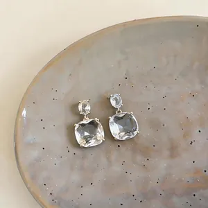 Close-up shot of elegant 18k gold-plated square zircon stud earrings on a ceramic plate