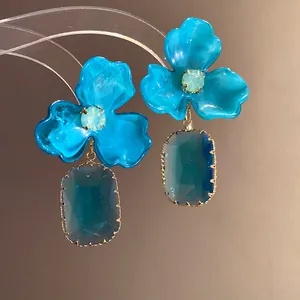Macro detail of blue acrylic flower earrings featuring dark blue gemstone pendants