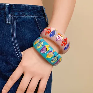 Close-up detail of resort style resin wide bangles with colorful tropical fish prints.