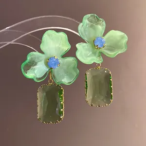 Macro view of green acrylic flower earrings with blue crystals and gemstone drops