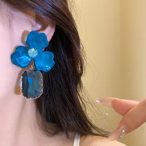Detailed close-up view of blue acrylic flower earrings with dark blue crystal drop pendant
