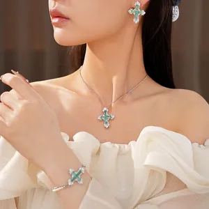 Elegant jewelry set with green gemstone cross necklace, earrings, and bracelet on model.