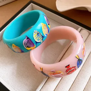 Close-up of resin wide bangles featuring vibrant tropical fish patterns in a jewelry box