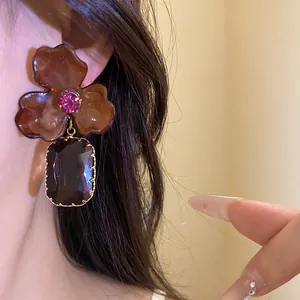Close-up detail of brown acrylic flower drop earrings featuring a dark crystal pendant