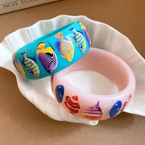Detail of wide resin bangles with colorful tropical fish prints in a shell