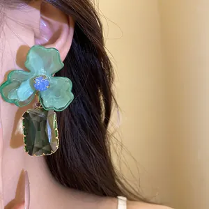 Close-up of a large green acrylic flower earring with a dark green crystal pendant