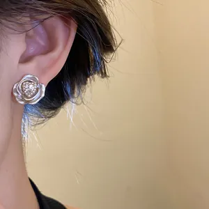 Close-up detail of a delicate silver flower earring with a heart-shaped crystal on an ear