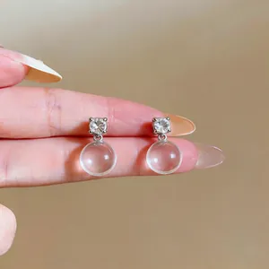 Close-up detail of silver stud earrings with sparkling zircon and clear glass round beads.