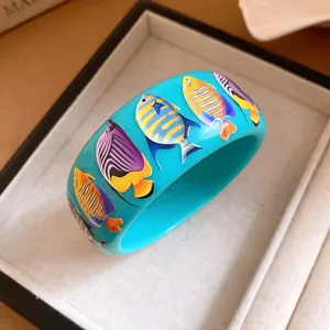 Close-up of wide blue resin bangle featuring vibrant tropical fish patterns in glossy finish.