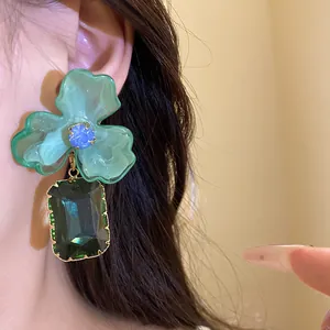 Detailed macro view of green acrylic flower earring with emerald crystal pendant.
