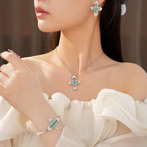 Detail shot of an elegant emerald-green zircon cross jewelry set worn by a model in soft light.